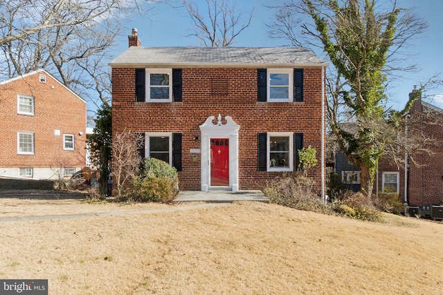 colonial house featuring a front yard, brick siding, and a chimney