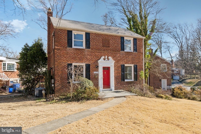 view of front of property with a chimney, central AC, and brick siding