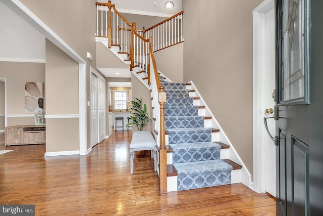 foyer entrance with a towering ceiling, light wood finished floors, baseboards, and stairway