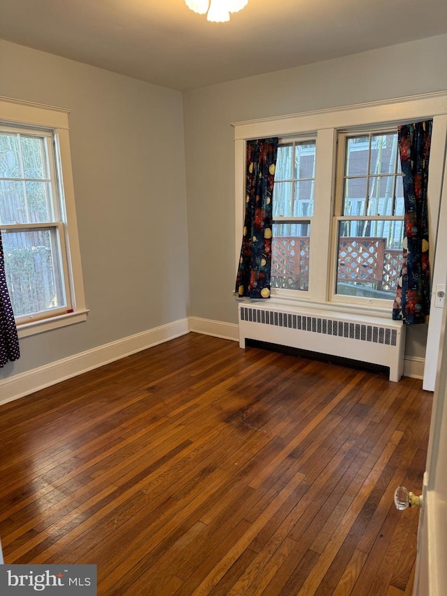 empty room featuring radiator, baseboards, and dark wood-type flooring