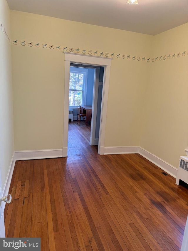 unfurnished room featuring radiator, wood finished floors, and baseboards