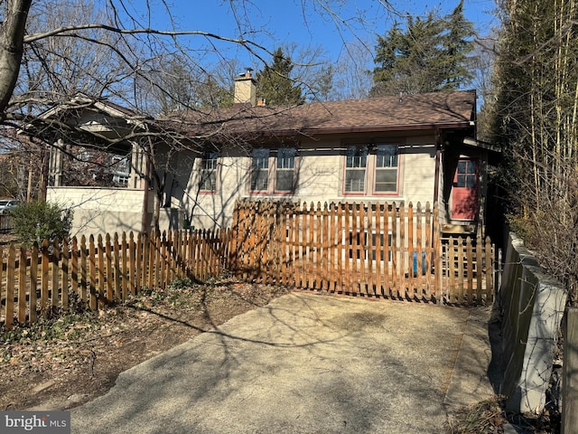 view of front facade featuring a fenced front yard, a chimney, and a shingled roof