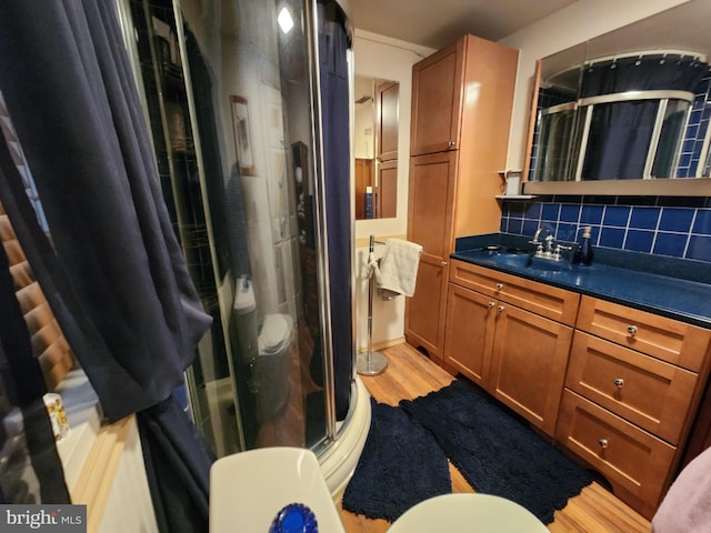 full bath featuring wood finished floors, a stall shower, backsplash, and vanity