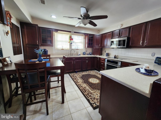 kitchen featuring backsplash, appliances with stainless steel finishes, glass insert cabinets, a sink, and dark brown cabinets