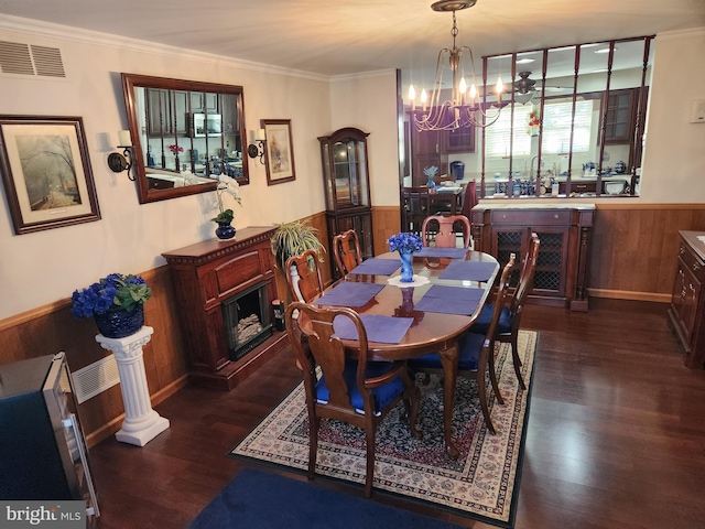 dining space with a wainscoted wall, ornamental molding, dark wood-style flooring, wood walls, and a notable chandelier