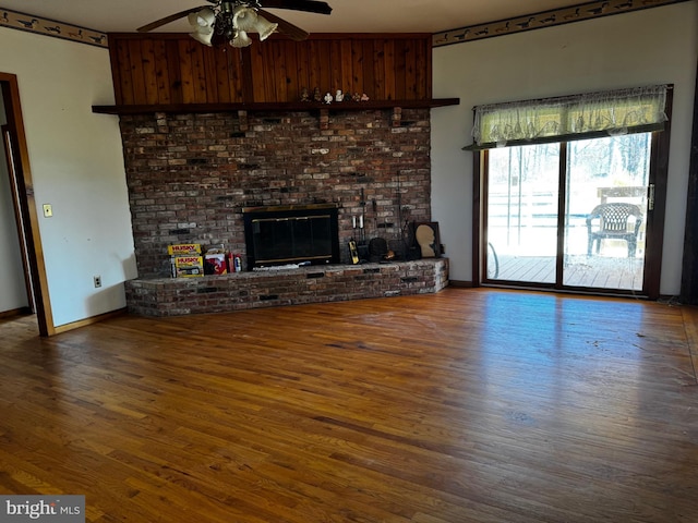 unfurnished living room with a brick fireplace, baseboards, wood finished floors, and ceiling fan