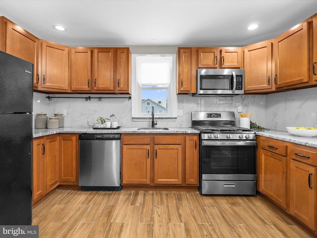 kitchen with appliances with stainless steel finishes, a sink, decorative backsplash, and light wood finished floors