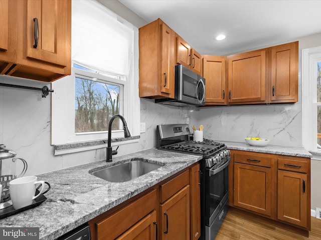 kitchen with tasteful backsplash, appliances with stainless steel finishes, light stone counters, and a sink