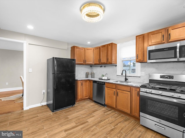 kitchen featuring a sink, appliances with stainless steel finishes, light wood-type flooring, decorative backsplash, and brown cabinetry