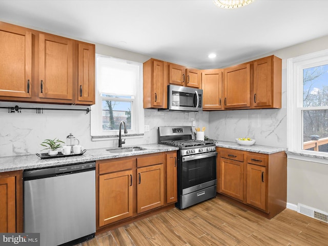 kitchen with stainless steel appliances, visible vents, light wood-style flooring, brown cabinetry, and a sink