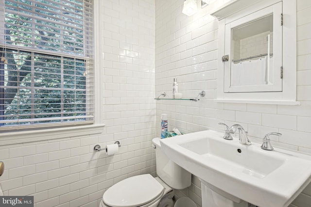 bathroom with a sink, toilet, and tile walls