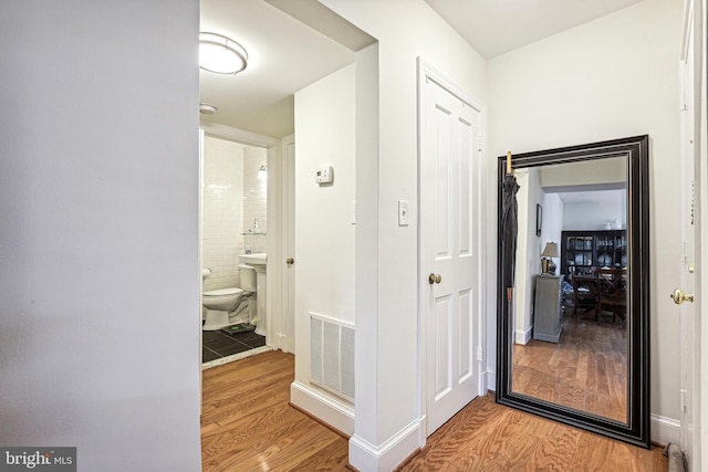 hallway with light wood-style flooring, visible vents, and baseboards