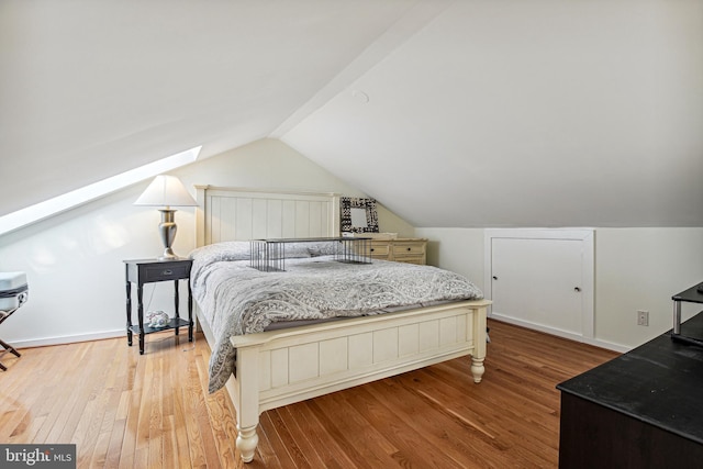 bedroom featuring vaulted ceiling with skylight, baseboards, and wood finished floors