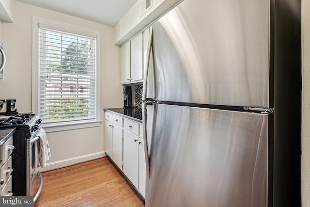 kitchen featuring appliances with stainless steel finishes, dark countertops, light wood-type flooring, and white cabinetry