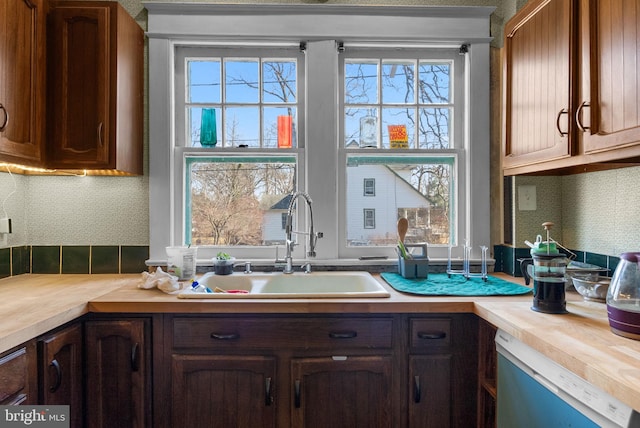 kitchen featuring wooden counters, white dishwasher, a sink, and decorative backsplash