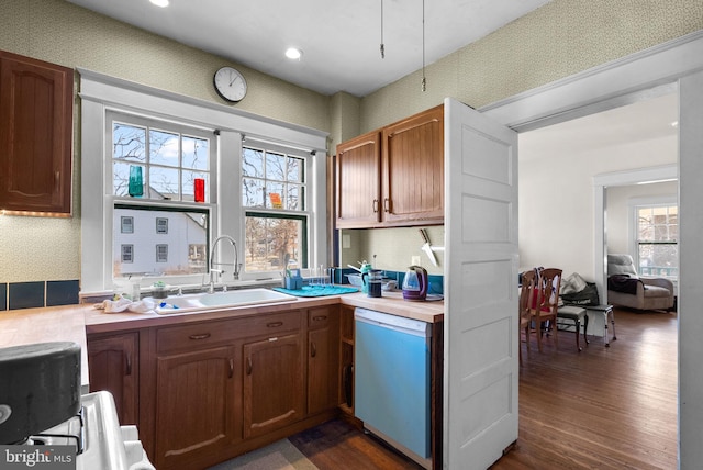 kitchen featuring dark wood-style flooring, light countertops, a sink, dishwasher, and wallpapered walls