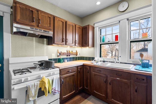 kitchen with wallpapered walls, light countertops, white gas stove, under cabinet range hood, and a sink