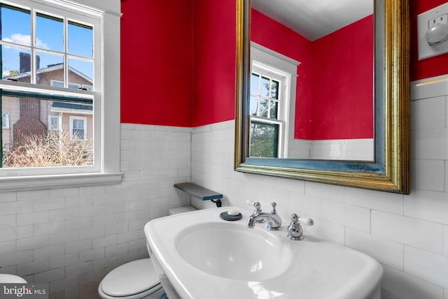 half bath with a sink, toilet, and tile walls