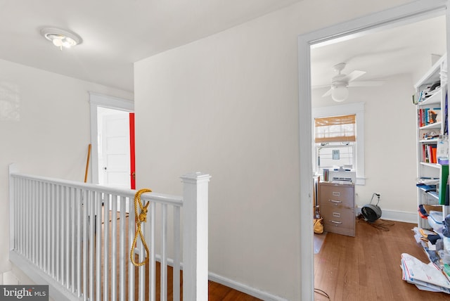 corridor with baseboards, an upstairs landing, and wood finished floors