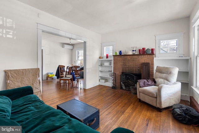 living room featuring a brick fireplace, a wall mounted air conditioner, baseboards, and wood finished floors