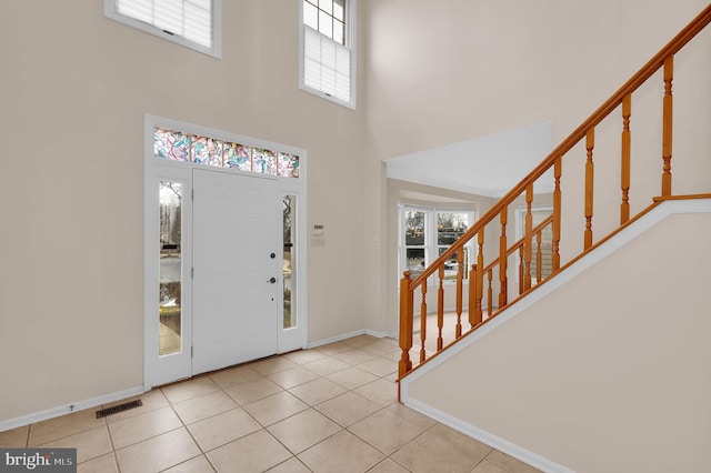 tiled foyer entrance featuring baseboards, visible vents, stairway, and a high ceiling