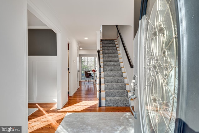 foyer featuring a decorative wall, wood finished floors, ornamental molding, stairway, and wainscoting