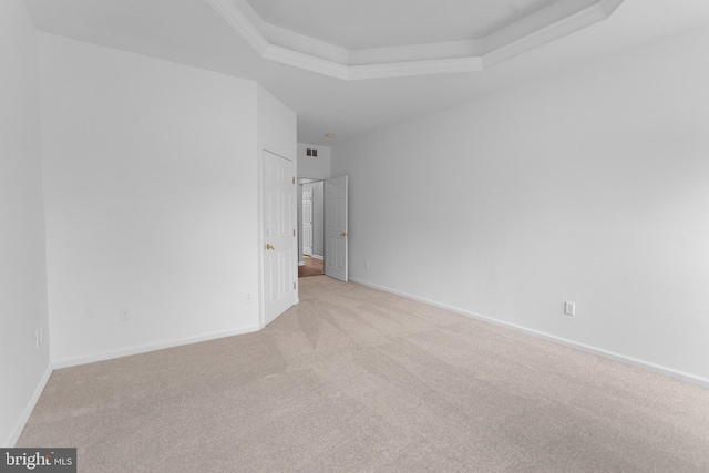 spare room featuring light colored carpet, visible vents, baseboards, ornamental molding, and a raised ceiling