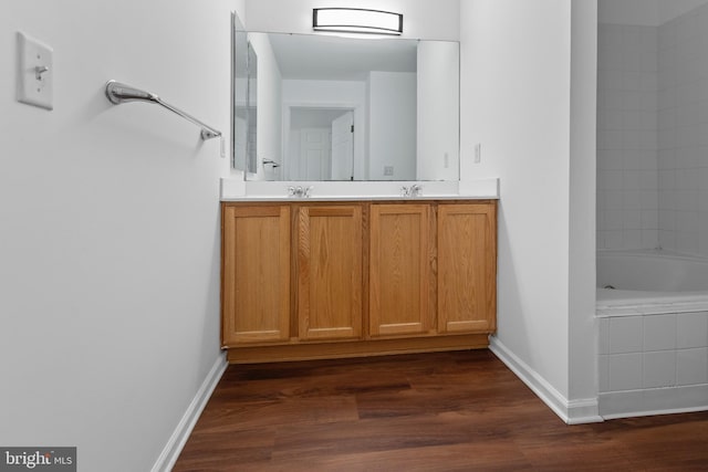 bathroom featuring double vanity, a bathing tub, baseboards, and wood finished floors