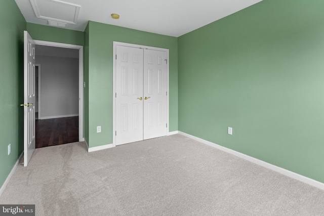 unfurnished bedroom featuring a closet, carpet flooring, attic access, and baseboards