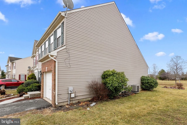 view of side of property with aphalt driveway, an attached garage, a yard, central AC, and brick siding