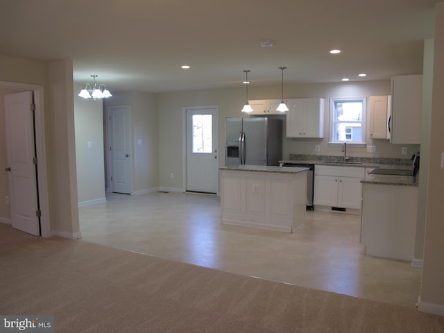 kitchen with a kitchen island, a sink, white cabinetry, appliances with stainless steel finishes, and decorative light fixtures