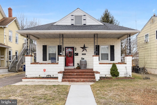 bungalow with a front yard, covered porch, roof with shingles, and stairway