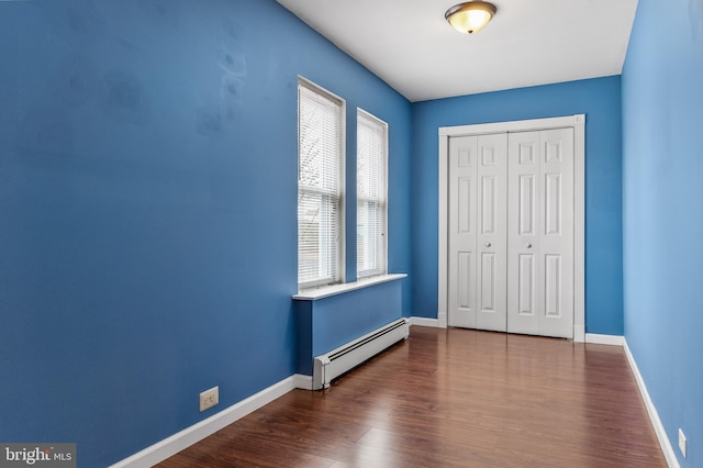 unfurnished bedroom featuring a closet, baseboard heating, wood finished floors, and baseboards