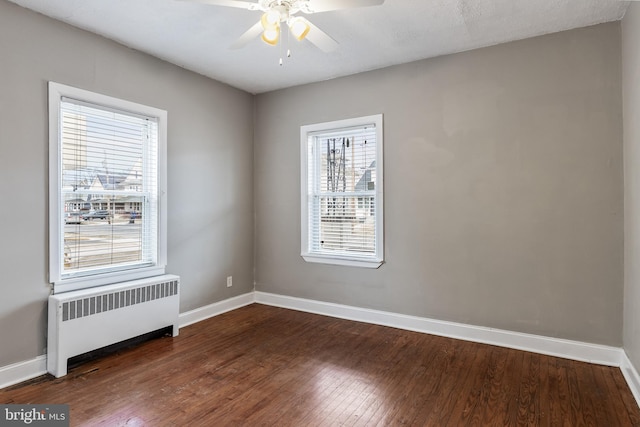 empty room featuring dark wood-style floors, radiator, baseboards, and a ceiling fan