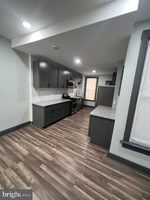 kitchen featuring stainless steel appliances, dark wood-type flooring, baseboards, dark cabinetry, and light stone countertops