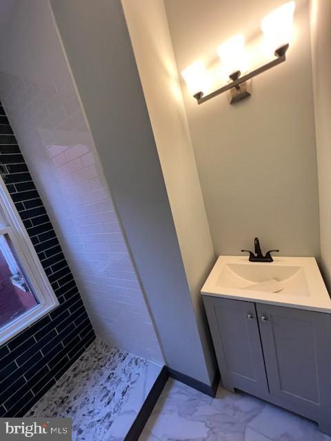 full bathroom with marble finish floor, a tile shower, and vanity