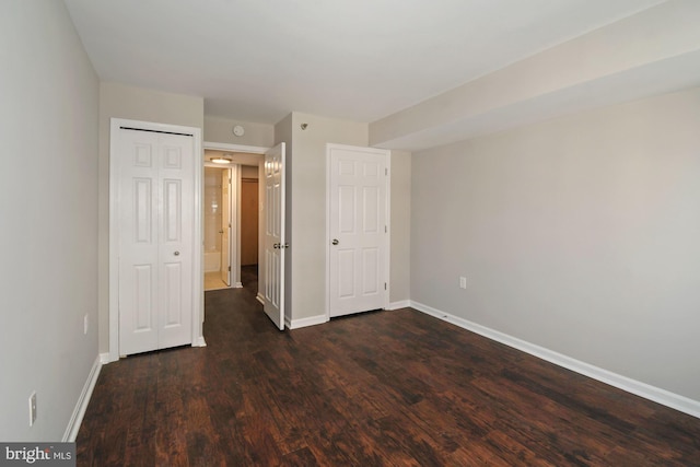 unfurnished bedroom featuring a closet, baseboards, and dark wood-style floors