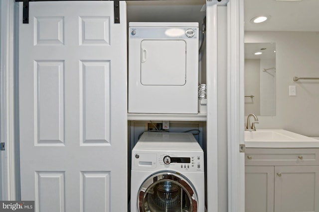 laundry area with laundry area, recessed lighting, a sink, a barn door, and stacked washer / dryer