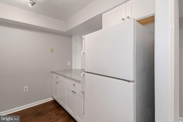 kitchen featuring light stone counters, dark wood finished floors, white cabinetry, freestanding refrigerator, and baseboards