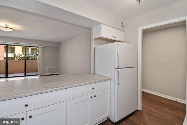 kitchen with light stone countertops, dark wood-style floors, visible vents, freestanding refrigerator, and white cabinetry