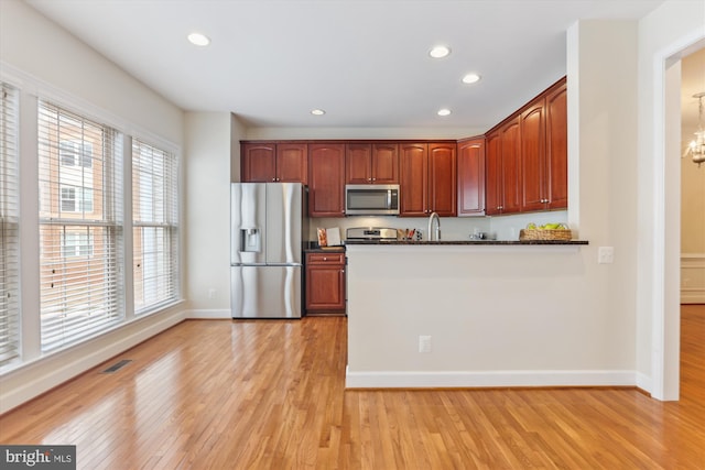 kitchen featuring visible vents, dark countertops, light wood-style floors, appliances with stainless steel finishes, and a peninsula