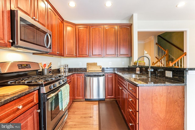 kitchen featuring a sink, dark stone countertops, appliances with stainless steel finishes, a peninsula, and light wood finished floors