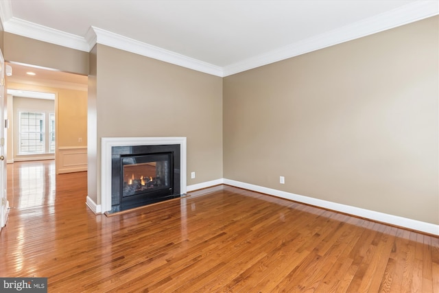 unfurnished living room with baseboards, a fireplace with flush hearth, wood finished floors, and crown molding