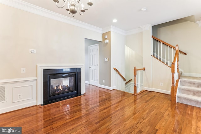 unfurnished living room featuring a chandelier, ornamental molding, baseboards, and wood finished floors