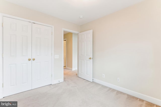 unfurnished bedroom featuring baseboards, a closet, and light carpet