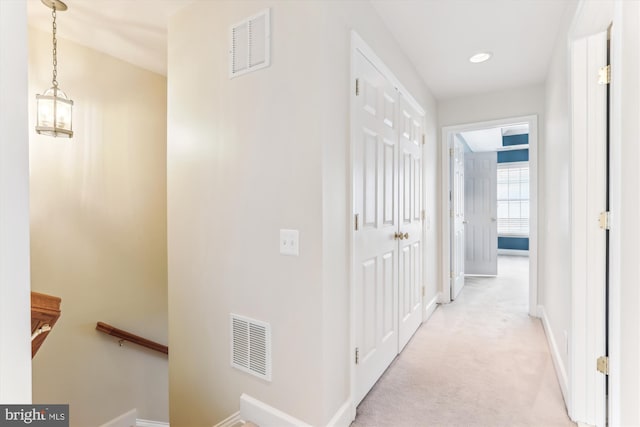 corridor featuring an upstairs landing, light colored carpet, visible vents, and baseboards