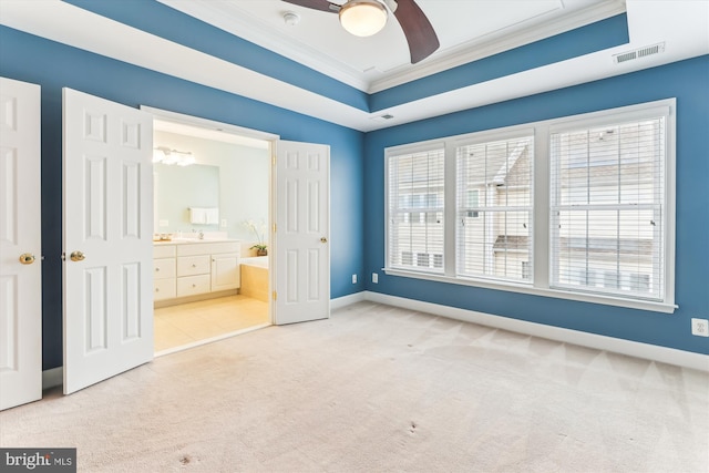 unfurnished bedroom featuring baseboards, visible vents, a tray ceiling, ornamental molding, and light carpet