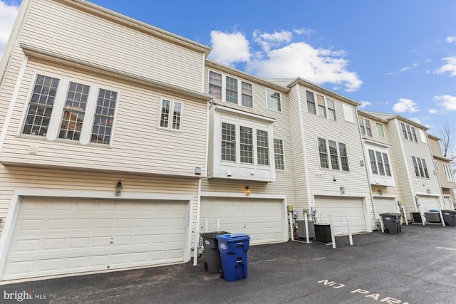 rear view of property featuring central AC unit, an attached garage, and driveway