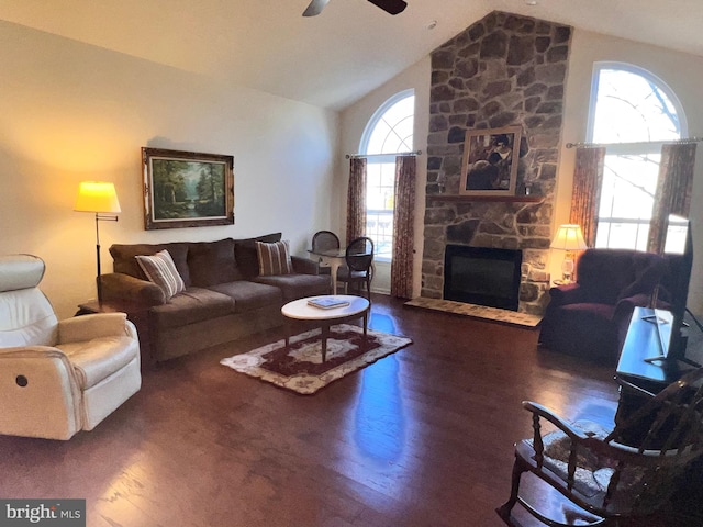 living room featuring high vaulted ceiling, dark wood finished floors, a stone fireplace, and ceiling fan