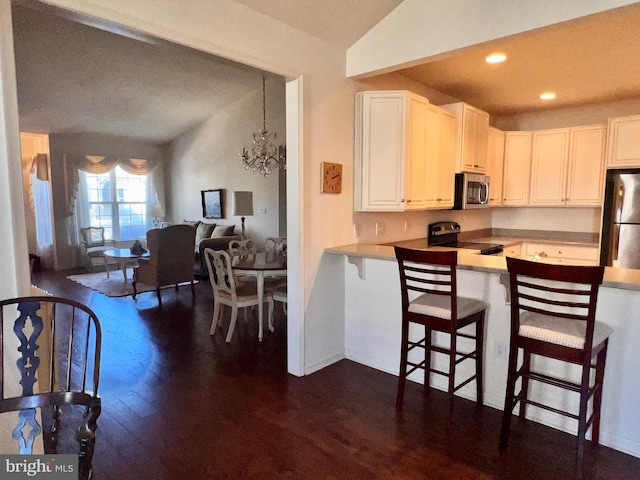 kitchen featuring appliances with stainless steel finishes, open floor plan, a kitchen breakfast bar, a peninsula, and white cabinetry